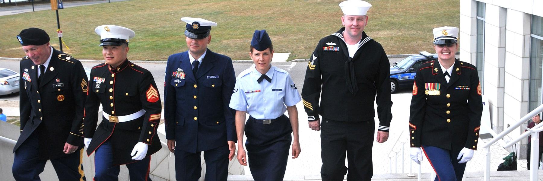 group of veterans in uniform walks up campus center steps.